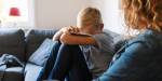 Child hiding face. Sitting in sofa with woman.