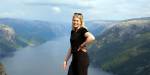 Portrait of Lara with a view of mountains and fjord in the background. It is overcast and partly cloudy.