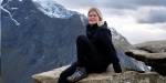 Portrait of Lara Janssen sitting on a rock high up in the mountains. Steep cliff and mountains in the background.