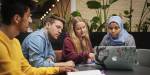 Four students working together with a laptop, around a table.