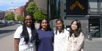 Gruppebilde av Nana Buabeng, Miriam Sarpong, Mathangi Murugesu og Kaja Reehorst. De er utendørs i solskinn en forsommerdag, med OsloMet-bygninger i bakgrunnen